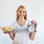 mulher segurando salada e relógio jejum intermitente