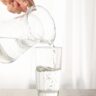 Derramar água fresca purificada no jarro de vidro na mesa de madeira.