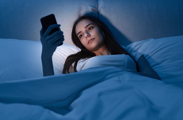 Jovem mulher com celular deitada na cama