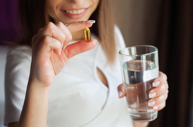 Mulher tomando medicamento via oral com copo de água fresca dentro de casa. 